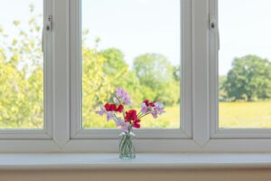 A vase of Mother's Day flowers sits in front of windows overlooking scenery.