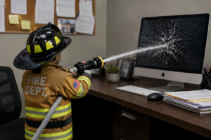 kid in fire fighter jacket spraying water at a computer monitor
