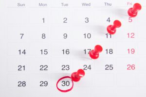 A wall calendar with red pushpins marking a trail of important dates leading to a circled date on the 30th, representing the importance of planning ahead for seasonal and holiday marketing campaigns.